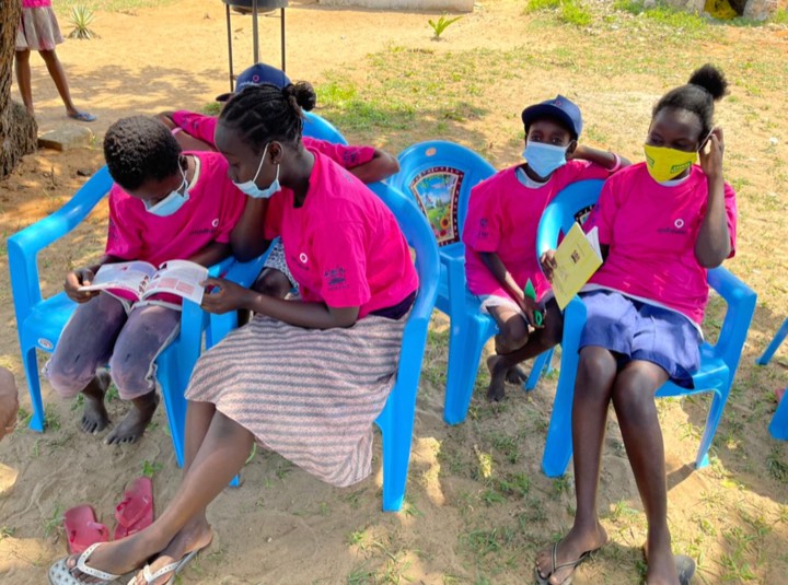 Girls in pink shirts seated outdoors reading health booklets